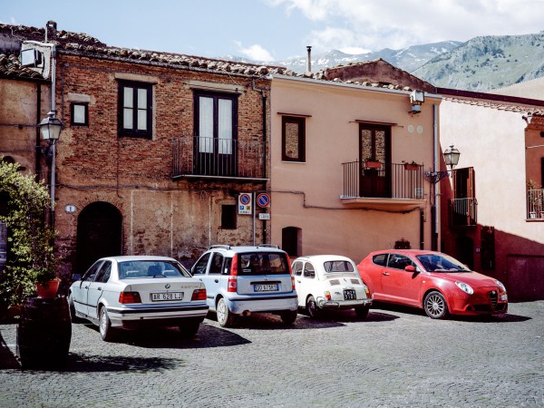 Drei Generationen italienischer Kennzeichen: links auf dem 3er BMW ein anonymisiertes Aluminium-Kennzeichen aus dem Zeitraum 1985-1994 ohne Provinzkürzel, daneben auf dem Fiat Panda 2 das 1999 eingeführte Euro-Kennzeichen. Der Fahrzeughalter hat hier zusätzlich die Möglichkeit, auf der rechten blauen Fläche das Provinzkürzel eintragen zu lassen. Auf dem Fiat 500L ein bis 1975 vergebenes Kunststoffkennzeichen mit Provinzkürzel (hier PA für Palermo). Zwischen 1976 und 1985 war auf diesem Kennzeichen-Typ das Provinzkürzel orangefarben. Castelbuono.