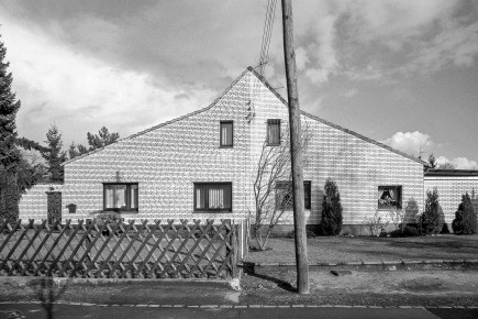Doppelhaus des Typs P, die häufigste Bauform in der Siedlung Rotes Haus. Das entlang der Firstlinie getrennte Doppelhaus mit seitlichem Stallanbau unter einem Schleppdach wurde durch Überbauung des Eingangsbereichs zur Straße hin erweitert. Auffällig die asymmetrische Platzierung und Größe der Fenster. Auch hier findet wie beim Nachbarhaus 1h die Stromversorgung oberirdisch statt.