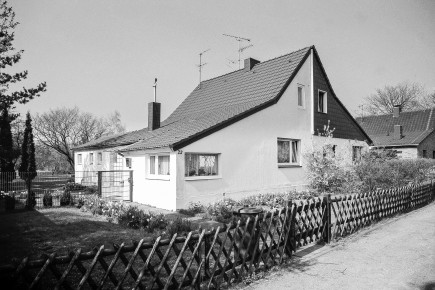 Für die Siedlung typische Wohnraumerweiterungen sind an diesem Gebäude gut zu erkennen. Das ursprüngliche Siedlungshaus Typ P erstreckte sich giebelseitig bis zum Knick im Dach. Seitlich unter einem Schleppdach befand sich ein kleiner Anbau mit Eingangstür, Arbeitszimmer, Stall und WC. Hier wurde der Anbau sowohl nach vorne bis zur Hausfront als auch nach hinten in den Garten verlängert. Weitere Ausbauten nach 1990 sind auf der Google Maps-Satellitenansicht zu erkennen. Ästhetisch problematisch wurde in späteren Jahren die Trennung des Haustyps P entlang der Firstlinie in 2 Wohneinheiten. Unterschiedliche nachträgliche Fassadengestaltungen oder Umbauten der beiden Haushälften führten zu einem unausgewogenem Erscheinungsbild der Häuser und der gesamten Siedlung.